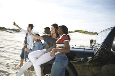 Junge Freunde mit Kameratelefonen machen ein Selfie am Jeep am sonnigen Strand - CAIF27183