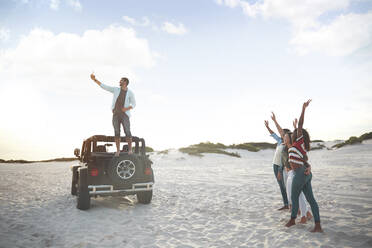 Junger Mann auf Jeep-Reifen macht Selfie mit Freunden am Strand - CAIF27188