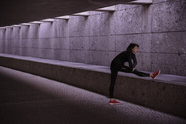 Female athlete warming up before running in pedestrian underpass - DHEF00165