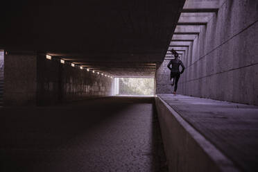 Female athlete running through pedestrian underpass - DHEF00173