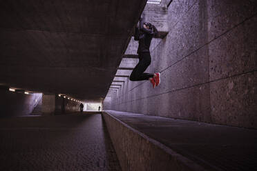 Female athlete working out in a pedestrian underpass, doing chin-ups - DHEF00179