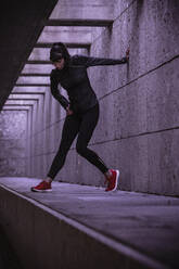 Female athlete warming up before running in pedestrian underpass - DHEF00182