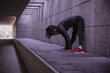 Sportlerin beim Aufwärmen vor einem Lauf in einer Fußgängerunterführung - DHEF00183