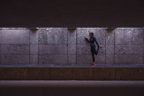Sportlerin beim Aufwärmen vor einem Lauf in einer Fußgängerunterführung - DHEF00186