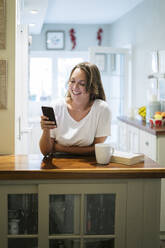 Junge Frau benutzt Smartphone in der Küche - MPPF00868
