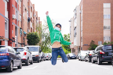 Boy wearing protective mask and jumping on a street - JCMF00683