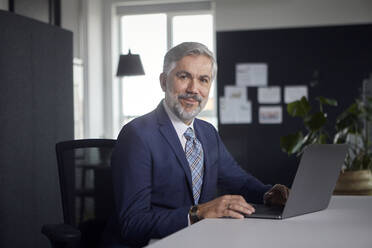 Portrait of mature businessman using laptop in office - RBF07668