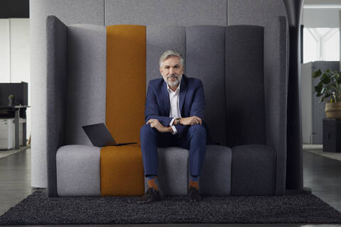 Porträt eines reifen Geschäftsmannes, der auf einer Couch im Büro sitzt, lizenzfreies Stockfoto
