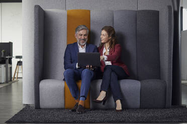Geschäftsfrau und Geschäftsmann sitzen auf einer Couch im Büro und teilen sich einen Laptop - RBF07682