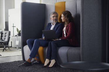 Businesswoman and businessman sitting on couch in office sharing laptop - RBF07683