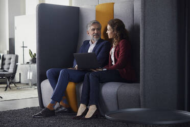 Geschäftsfrau und Geschäftsmann sitzen auf einer Couch im Büro und teilen sich einen Laptop - RBF07683