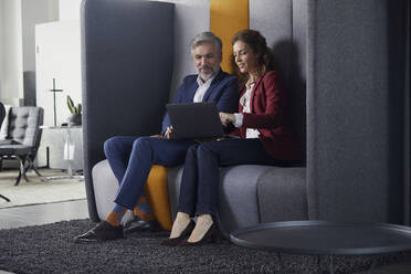 Businesswoman and businessman sitting on couch in office sharing laptop - RBF07684