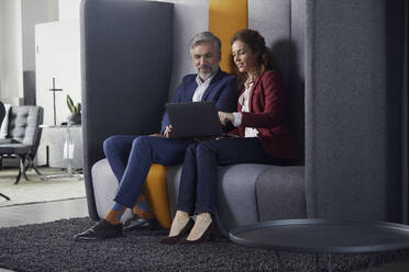 Geschäftsfrau und Geschäftsmann sitzen auf einer Couch im Büro und teilen sich einen Laptop - RBF07684