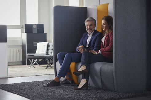 Geschäftsfrau und Geschäftsmann sitzen auf einer Couch im Büro und teilen sich einen Laptop - RBF07685