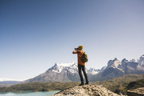 Wanderer in einer Berglandschaft, der durch ein Fernglas auf den Lago Pehoe im Torres del Paine National Park schaut, Patagonien, Chile - UUF20235