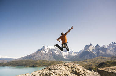 Hiker jumping in mountainscape at Lago Pehoe in Torres del Paine National Park, Patagonia, Chile - UUF20241