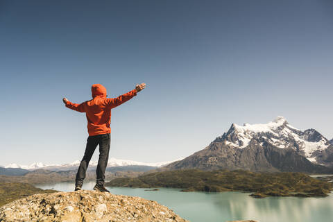 Wanderer mit erhobenen Armen in einer Berglandschaft am Lago Pehoe im Torres del Paine National Park, Patagonien, Chile, lizenzfreies Stockfoto