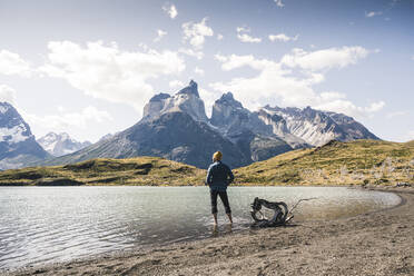Hiker in mountainscape wading in a lake in Torres del Paine National Park, Patagonia, Chile - UUF20249