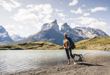 Glücklicher Mann in Berglandschaft am Seeufer im Nationalpark Torres del Paine, Patagonien, Chile - UUF20254