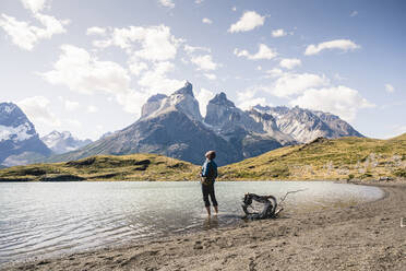 Hiker in mountainscape standing in a lake in Torres del Paine National Park, Patagonia, Chile - UUF20255