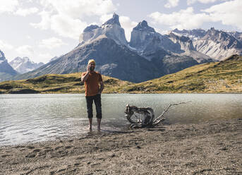 Man on the phone in mountainscape at lakeside in Torres del Paine National Park, Patagonia, Chile - UUF20258