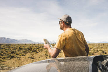 Rückansicht eines Mannes mit Landkarte am Auto in abgelegener Landschaft in Patagonien, Argentinien - UUF20277