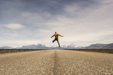 Mann springt auf eine Straße in abgelegener Landschaft in Patagonien, Argentinien - UUF20285