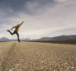 Mann springt auf eine Straße in abgelegener Landschaft in Patagonien, Argentinien - UUF20287