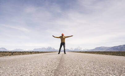 Mann mit ausgestreckten Armen steht auf einer Straße in abgelegener Landschaft in Patagonien, Argentinien - UUF20290