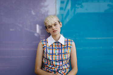 Portrait of female teenager wearing colorful dress leaning on multicolored glass wall - TCEF00552