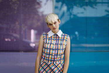 Portrait of female teenager wearing colorful dress leaning on multicolored glass wall - TCEF00553