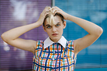 Portrait of female teenager with hand in hair wearing colorful dress with multicolored glass pane in the background - TCEF00554