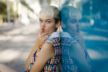 Portrait of female teenager grimacing wearing colorful dress leaning on multicolored glass pane - TCEF00561