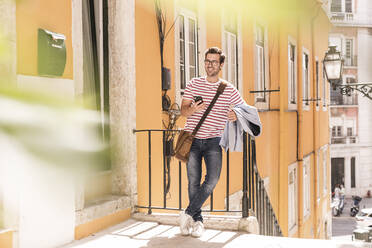 Smiling young man with smartphone in the city, Lisbon, Portugal - UUF20311