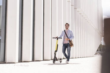 Young man with e-scooter and takeaway drink in the city, Lisbon, Portugal - UUF20316