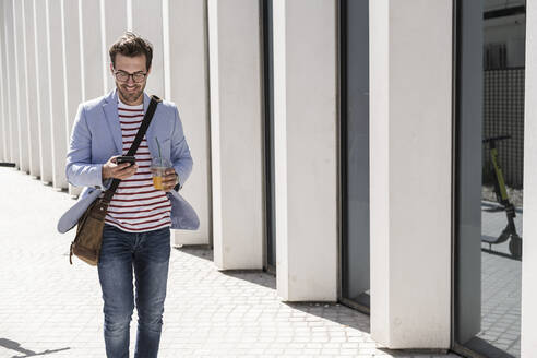 Young man walking in the city with cell phone and takeaway drink, Lisbon, Portugal - UUF20318