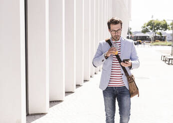 Young man in the city with cell phone and takeaway drink, Lisbon, Portugal - UUF20320