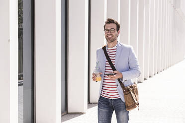 Smiling young man in the city with cell phone and takeaway drink, Lisbon, Portugal - UUF20322