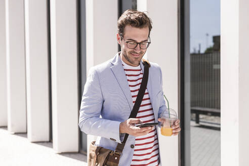 Junger Mann in der Stadt mit Mobiltelefon und Getränk zum Mitnehmen, Lissabon, Portugal - UUF20323