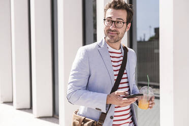 Junger Mann in der Stadt mit Mobiltelefon und Getränk zum Mitnehmen, Lissabon, Portugal - UUF20324