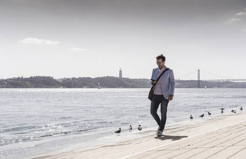 Young man walking on the waterfront using cell phone stock photo
