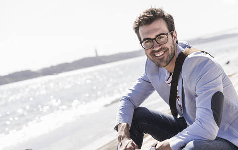 Portrait of happy young man sitting on the waterfront stock photo