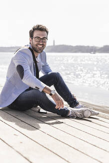 Porträt eines glücklichen jungen Mannes, der am Ufer sitzt - UUF20339