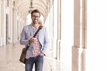 Portrait of smiling young man with smartphone in the city, Lisbon, Portugal - UUF20346