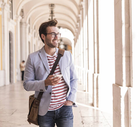 Lächelnder junger Mann mit Smartphone in der Stadt, Lissabon, Portugal, lizenzfreies Stockfoto