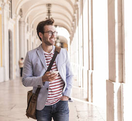Smiling young man with smartphone in the city, Lisbon, Portugal - UUF20347