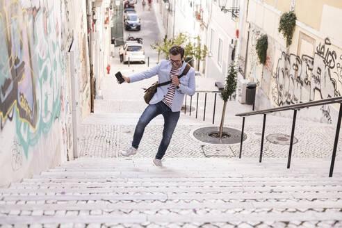 Unbekümmerter junger Mann auf einer Treppe in der Stadt, Lissabon, Portugal - UUF20353