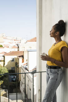 Junge Frau mit Kaffeetasse auf einem Balkon - UUF20364