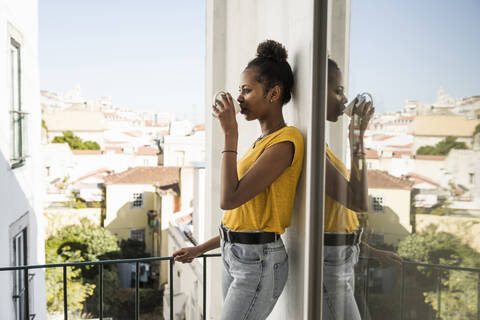 Junge Frau trinkt Kaffee auf einem Balkon, lizenzfreies Stockfoto