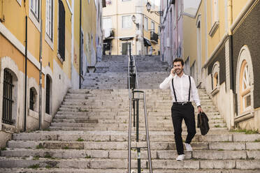 Lächelnder junger Mann am Telefon beim Treppensteigen in der Altstadt, Lissabon, Portugal - UUF20367
